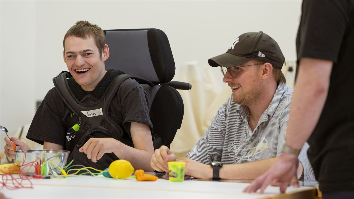 Ein Bewohner im Rollstuhl und ein Teammitglied lachen gemeinsam am Tisch.