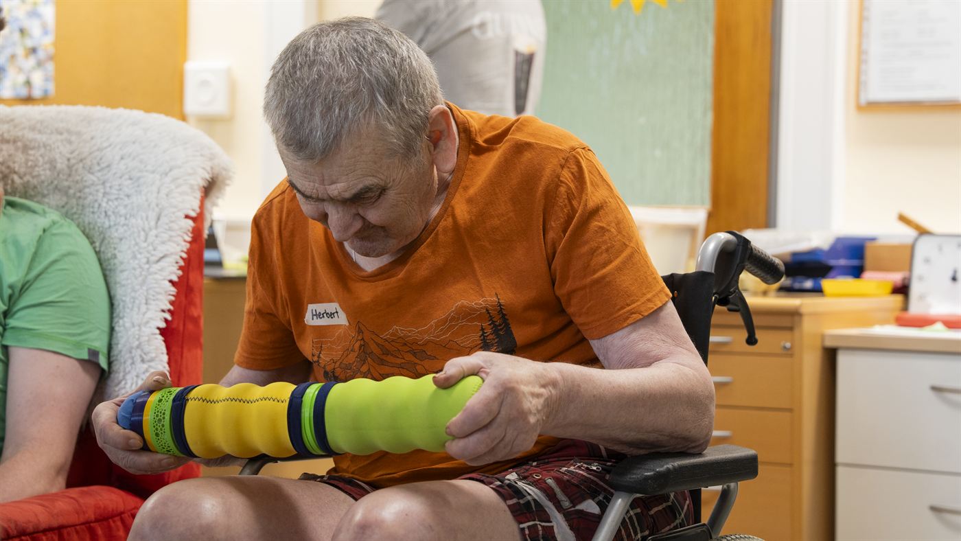 Ein Bewohner im orangefarbenen T-Shirt greift die Maupe mit beiden Händen.