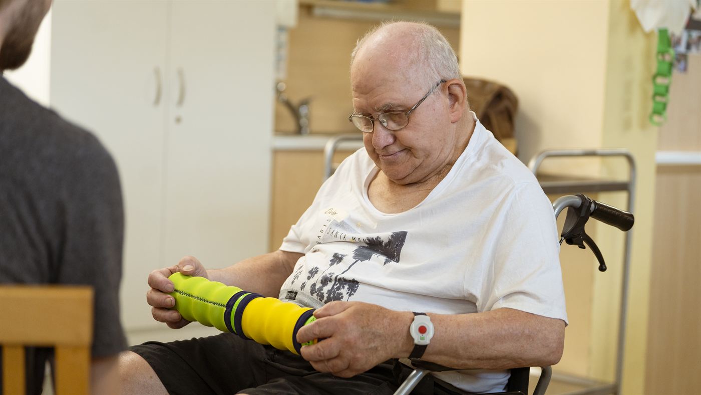 Ein älterer Bewohner mit Brille hält die Maupe prüfend in beiden Händen.