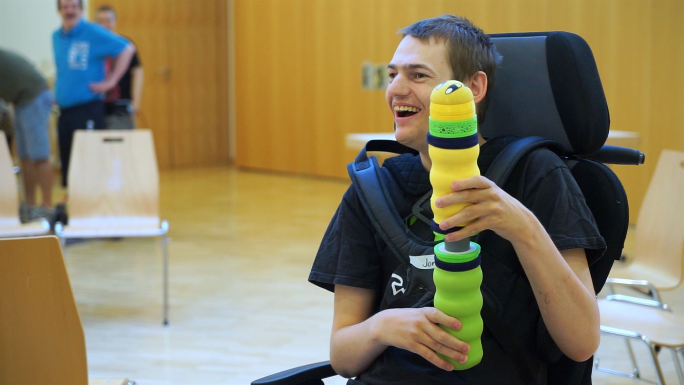 Der junge Bewohner hält die Maupe aufrecht neben sein Gesicht und lacht.